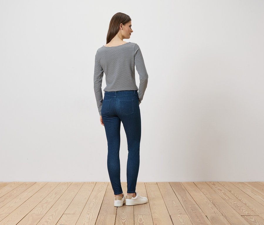 Une femme, vue de dos, porte un jean, un t-shirt rayé à manches longues et des baskets blanches.