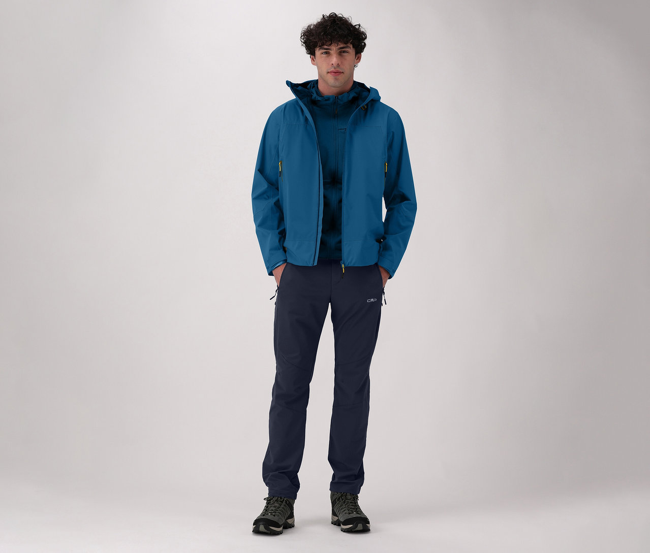 Homme portant une veste bleue et un pantalon de randonnée en nylon stretch CMP pour homme. Il se tient devant un fond clair.