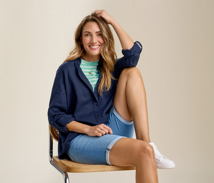 Femme assise sur une chaise portant un short en jean, un t-shirt et une blouse longue en lin bleu foncé.