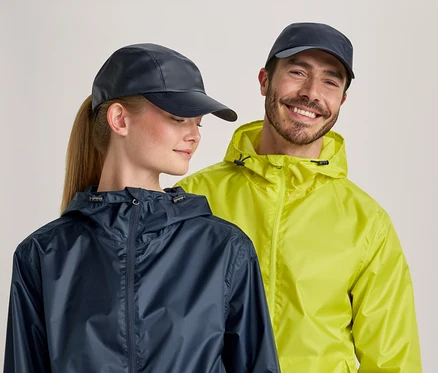 Une femme avec une queue de cheval et un homme avec une barbe portent des vestes de pluie bleues et jaune fluo et des casquettes bleues sur un fond clair.