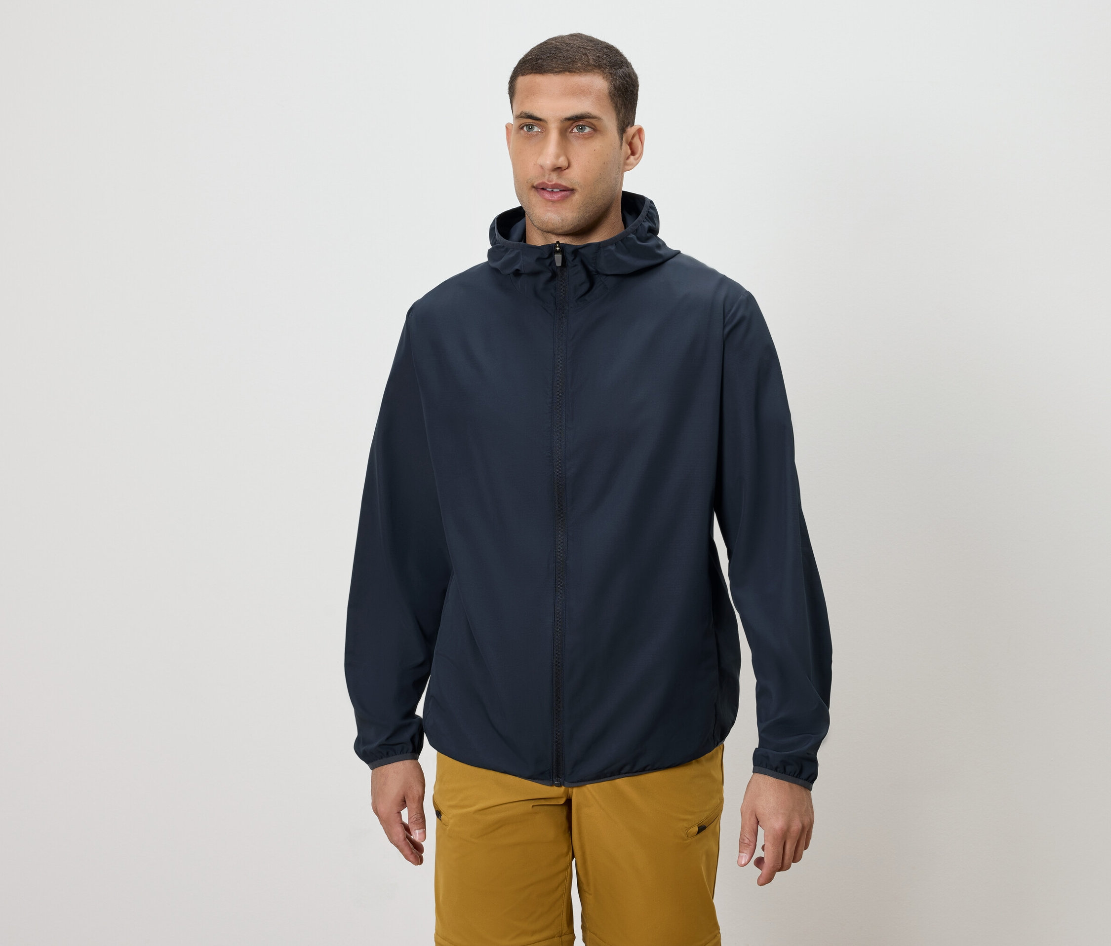 Un homme porte une veste à capuche bleu marine et un short doré.