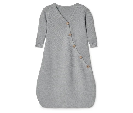 Une douillette pour bébé en tricot gris avec des manches longues et une fermeture à boutons repose sur une surface blanche.