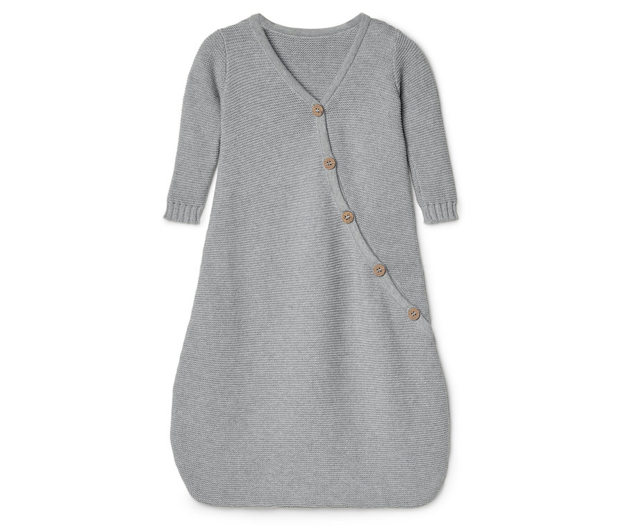 Une douillette pour bébé en tricot gris avec des manches longues et une fermeture à boutons repose sur une surface blanche.