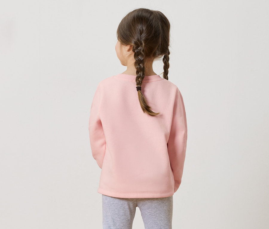Vue arrière d'une fillette avec des tresses portant un pull rose et un legging gris.