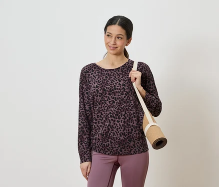 Femme portant un haut léopard violet et noir et un legging violet, tenant un tapis de yoga roulé sur l'épaule.