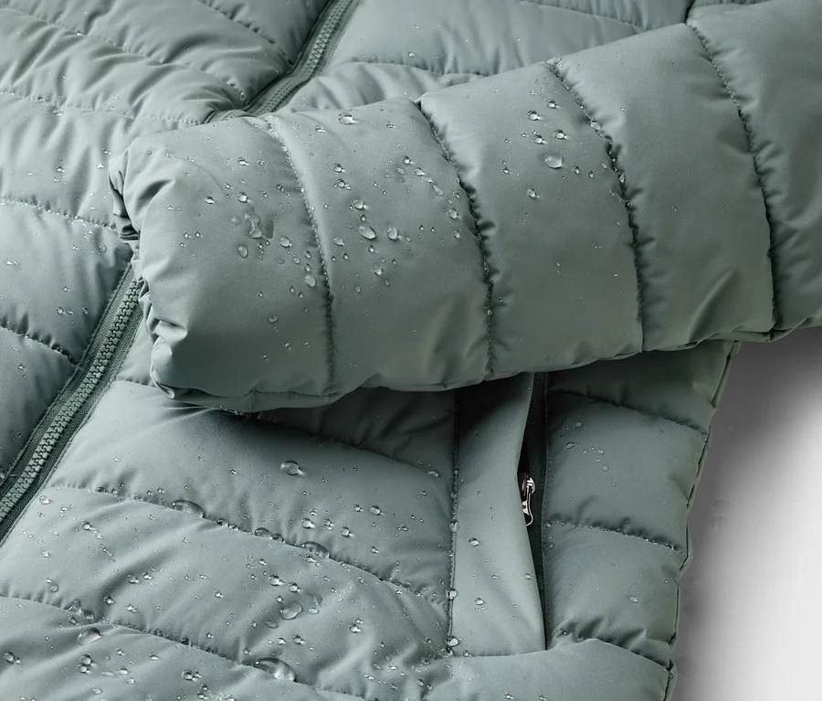 Gros plan d'une veste matelassée vert clair hydrofuge avec fermeture éclair et gouttes.