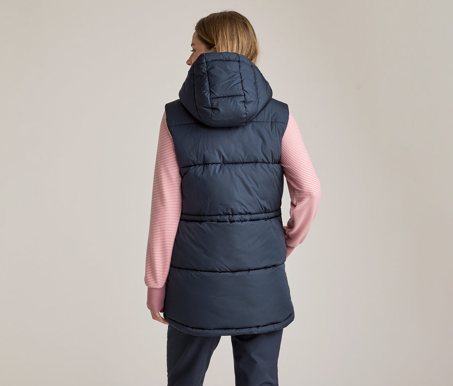 Femme vue de dos, portant une veste matelassée bleu marine à capuche sur un t-shirt à manches longues rayé rose et blanc et un pantalon foncé.