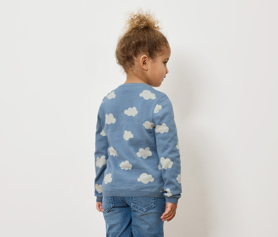 Enfant vu de dos, portant un pull bleu à motifs de nuages et un jean.