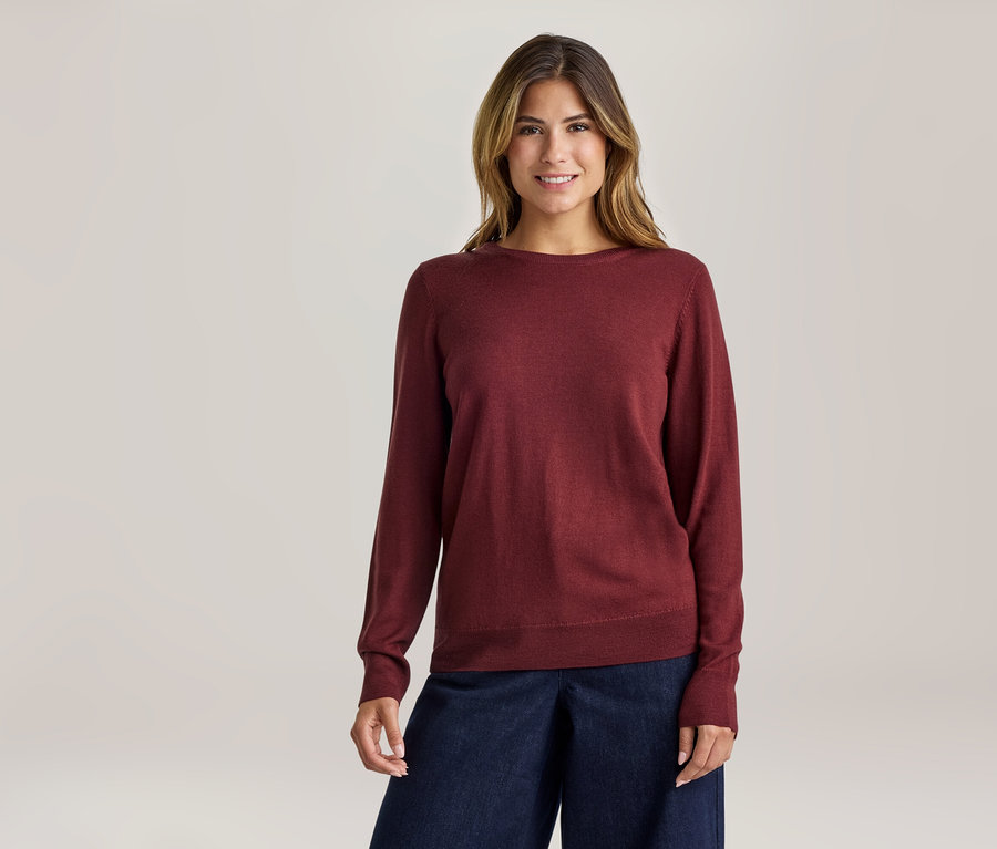 Femme souriante portant un pull rouge à manches longues et un pantalon large bleu foncé.