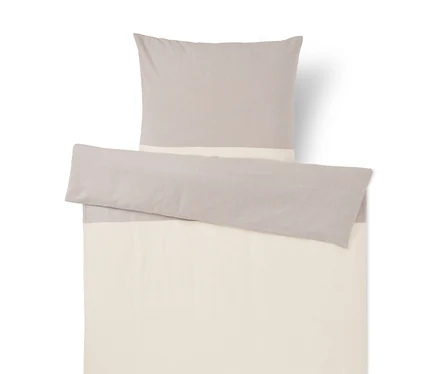 Parure de lit bicolore gris clair et crème. Un oreiller et une housse de couette pliée avec un motif color block.