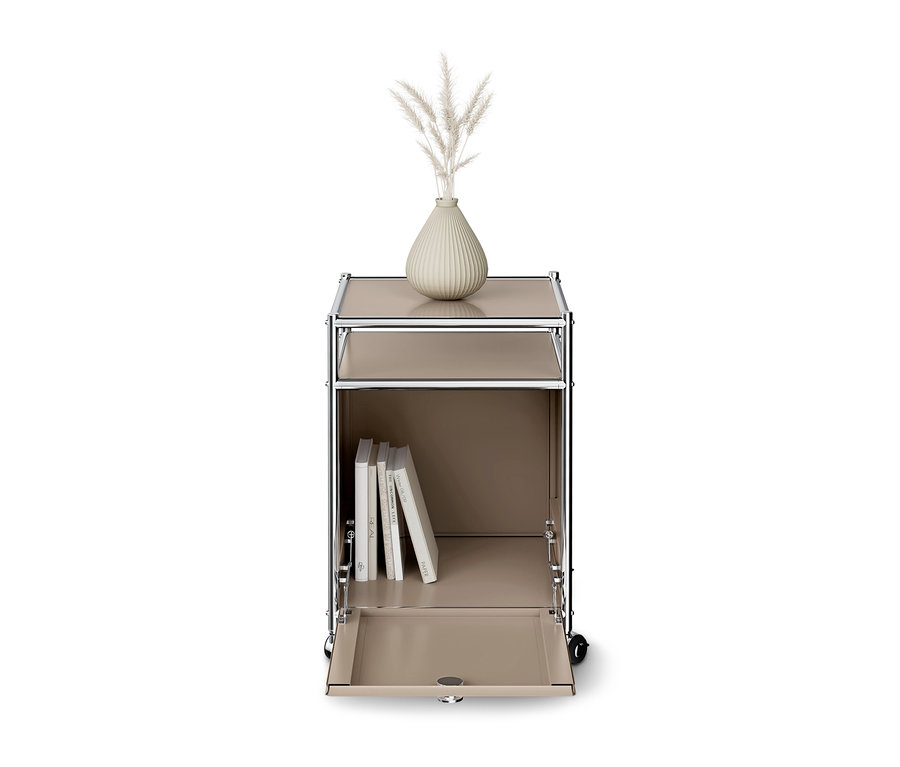 Meuble de rangement modulaire beige sur roulettes avec cadre chromé. Un vase avec des herbes séchées est posé dessus, le compartiment inférieur est ouvert et contient des livres.