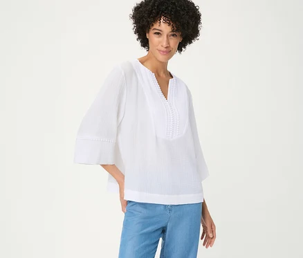 Femme souriante aux cheveux bouclés portant une blouse tissée Olsen blanche à col en V avec broderie et manches 3/4, et un jean bleu.