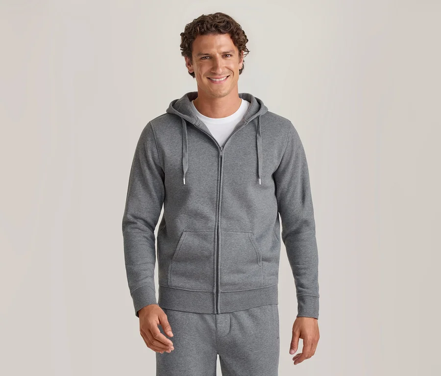 Homme souriant portant un sweat à capuche gris zippé sur un t-shirt blanc et un pantalon de jogging gris assorti.