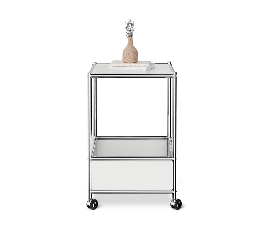 Table basse en métal CN3 blanche sur roulettes, avec plateau en verre, un tiroir blanc, des livres et un vase.