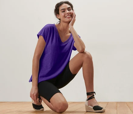 Une femme agenouillée sur un plancher en bois portant un t-shirt violet en mélange avec modal.