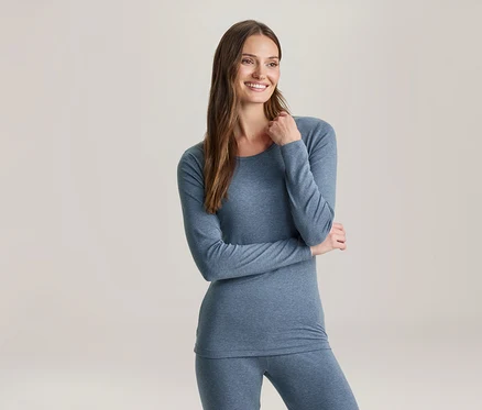 Une femme souriante aux longs cheveux bruns porte un haut bleu à manches longues et un legging assorti, regardant vers la droite.