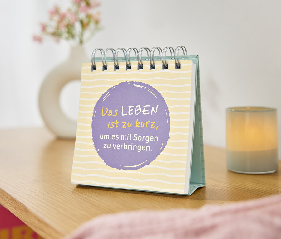 Calendrier de table avec la citation "La vie est trop courte pour être vécue avec des soucis" devant un vase et une bougie.