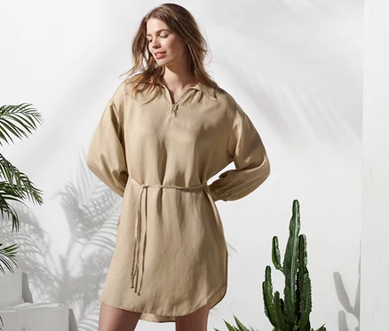 Une femme debout pose, portant une blouse longue beige en lin mélangé.