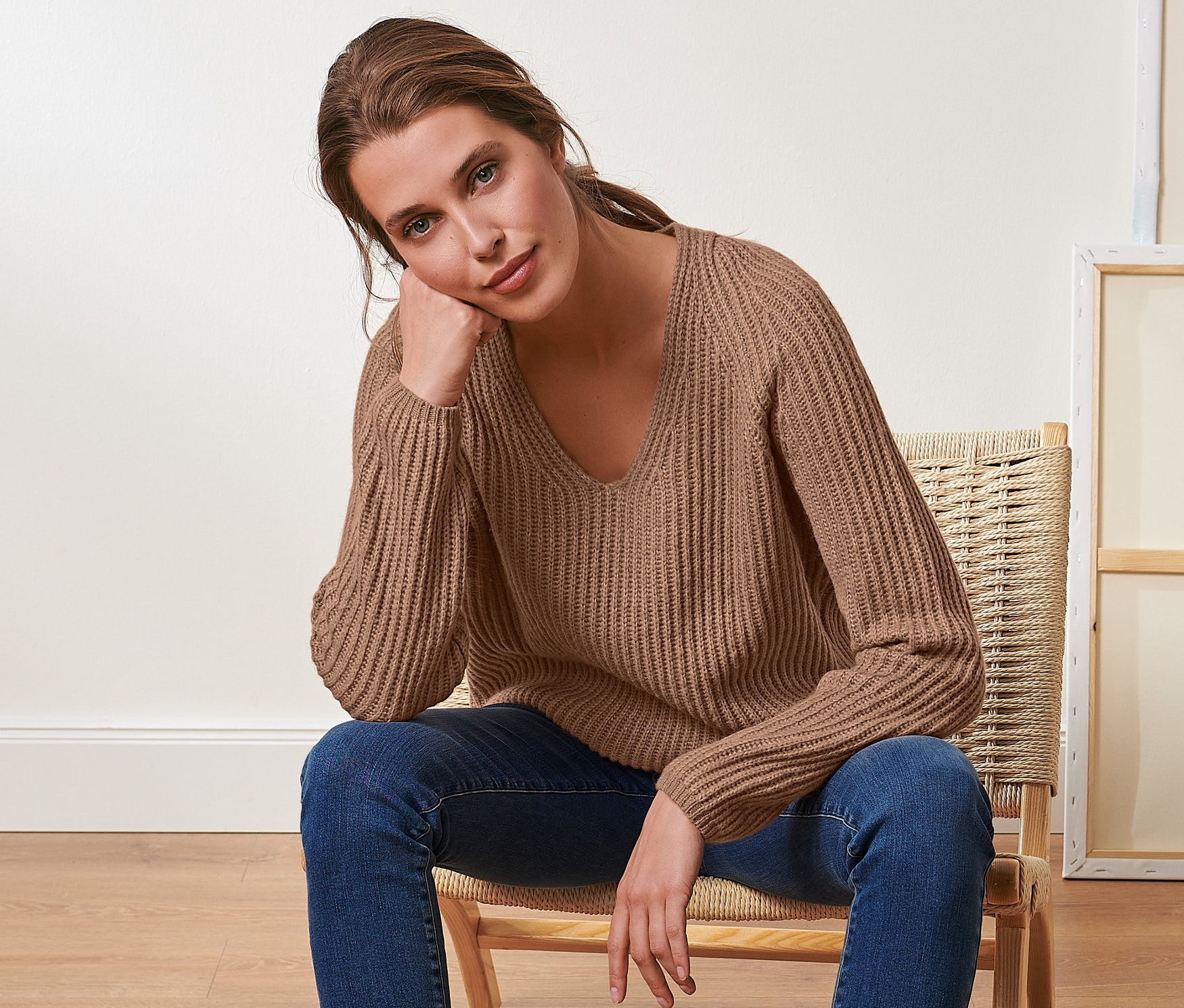 Femme assise sur une chaise portant un pull beige en grosse maille avec de la laine.