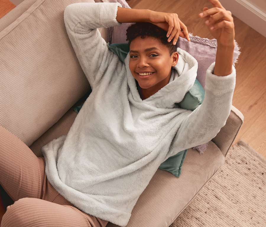 Une femme est allongée sur un canapé beige et porte un sweat à capuche moelleux.