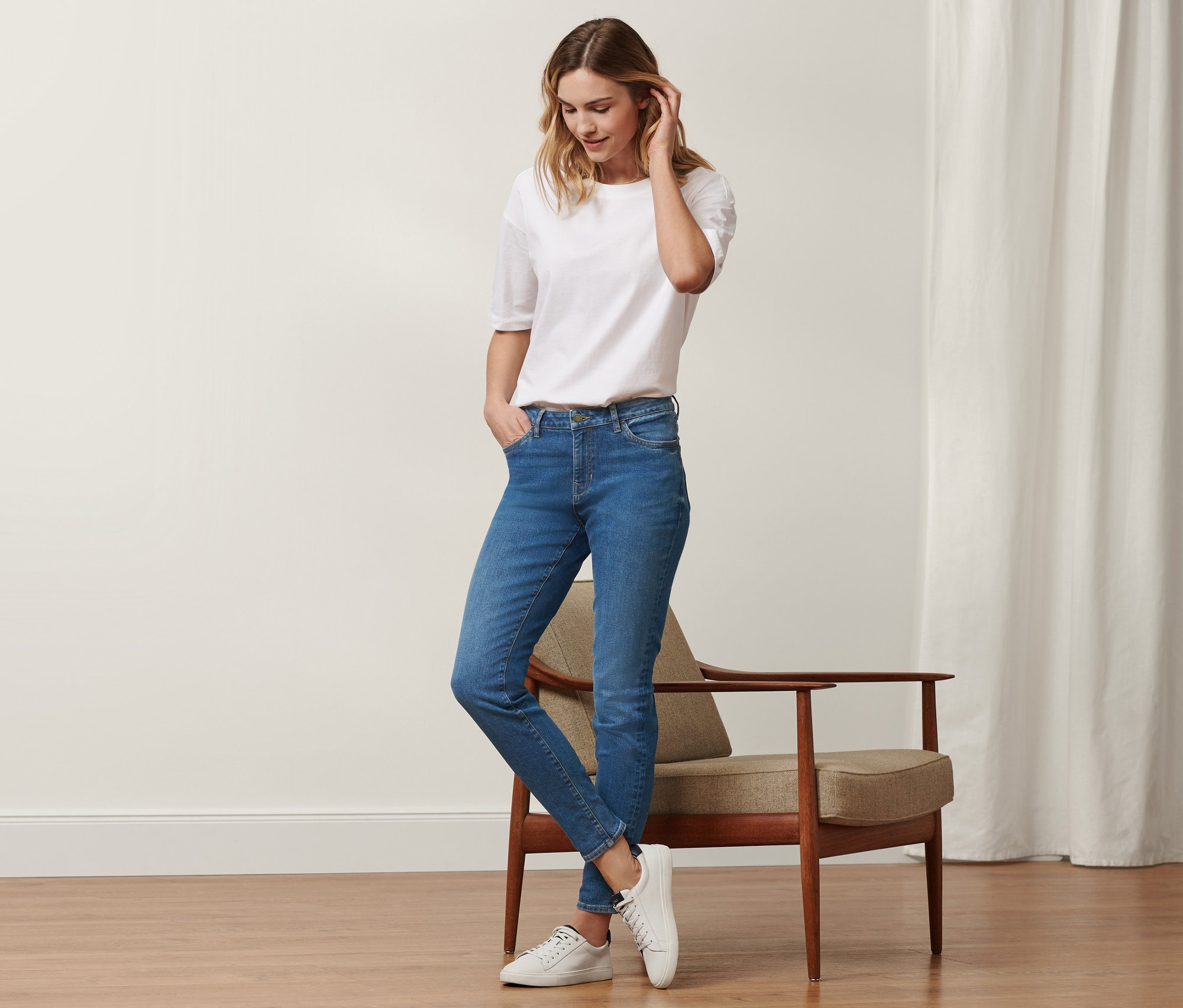 Une femme debout porte un jean slim en denim « Fit Emma » bleu moyen et un t-shirt blanc.