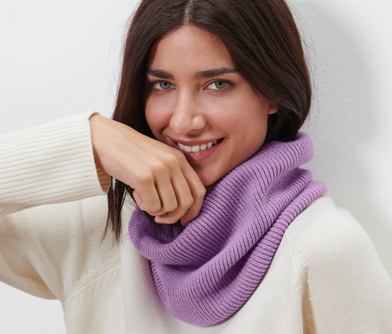 Une femme brune souriante porte une écharpe tube en maille.