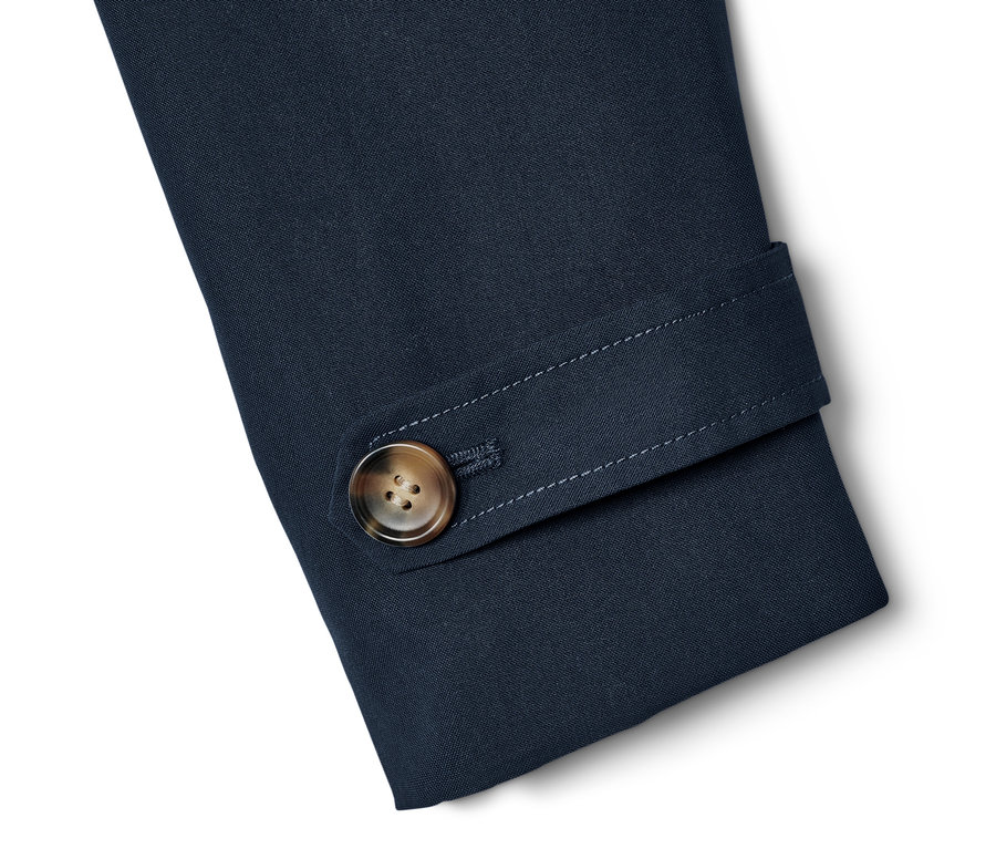 Détail de la manche d'un trench-coat bleu marine avec un bouton marron.