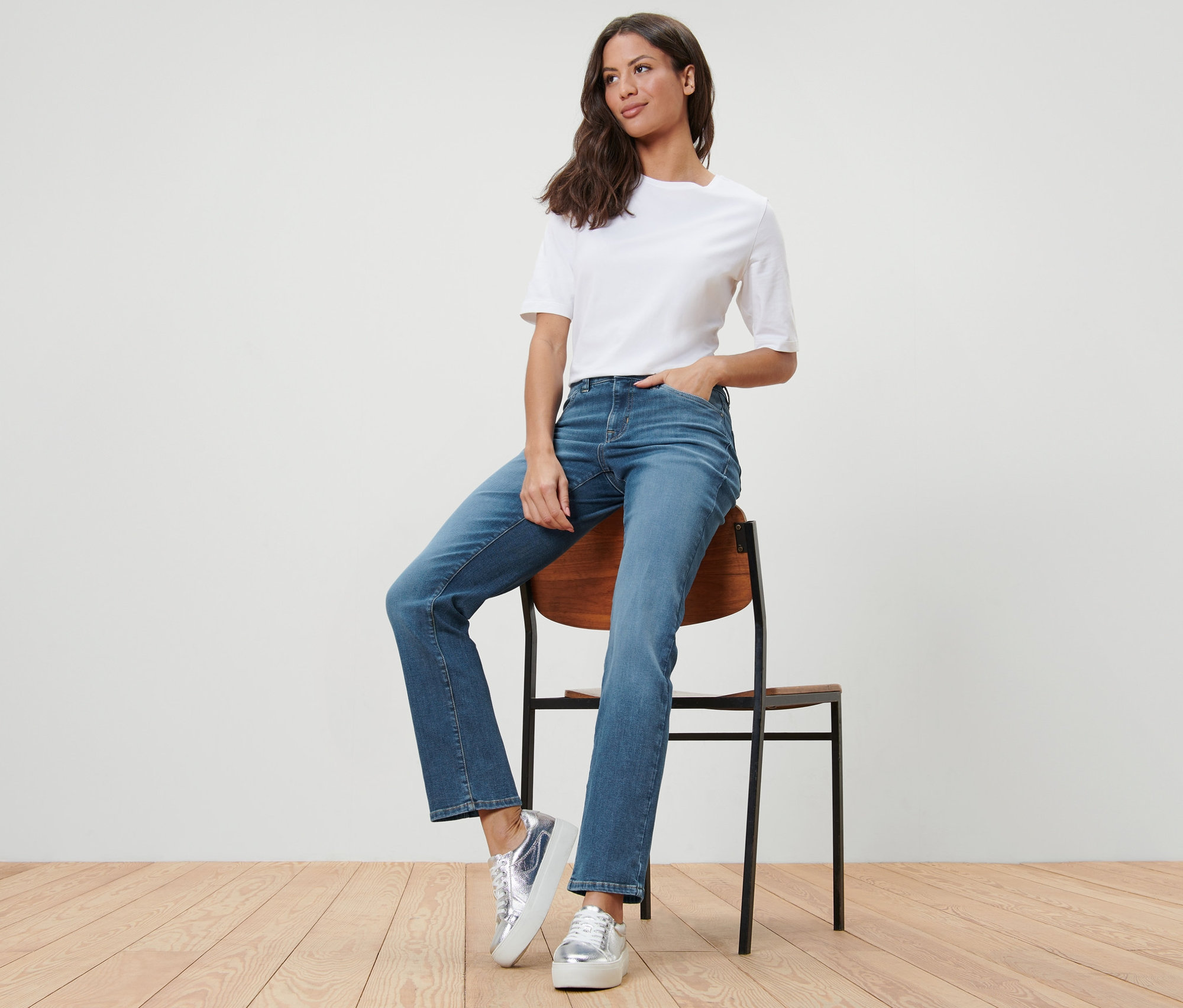 Femme assise sur une chaise portant un jean droit – Fit « Kira » et un t-shirt blanc.