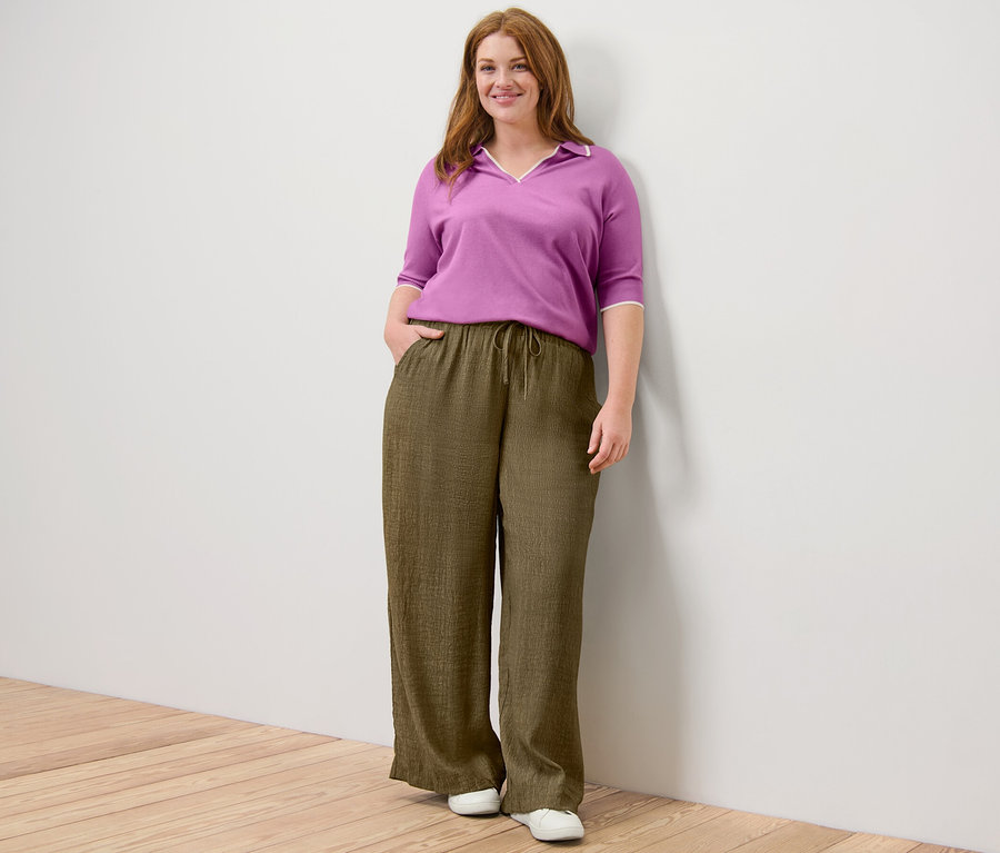 Femme posant en pantalon à taille élastique et polo en maille fine.