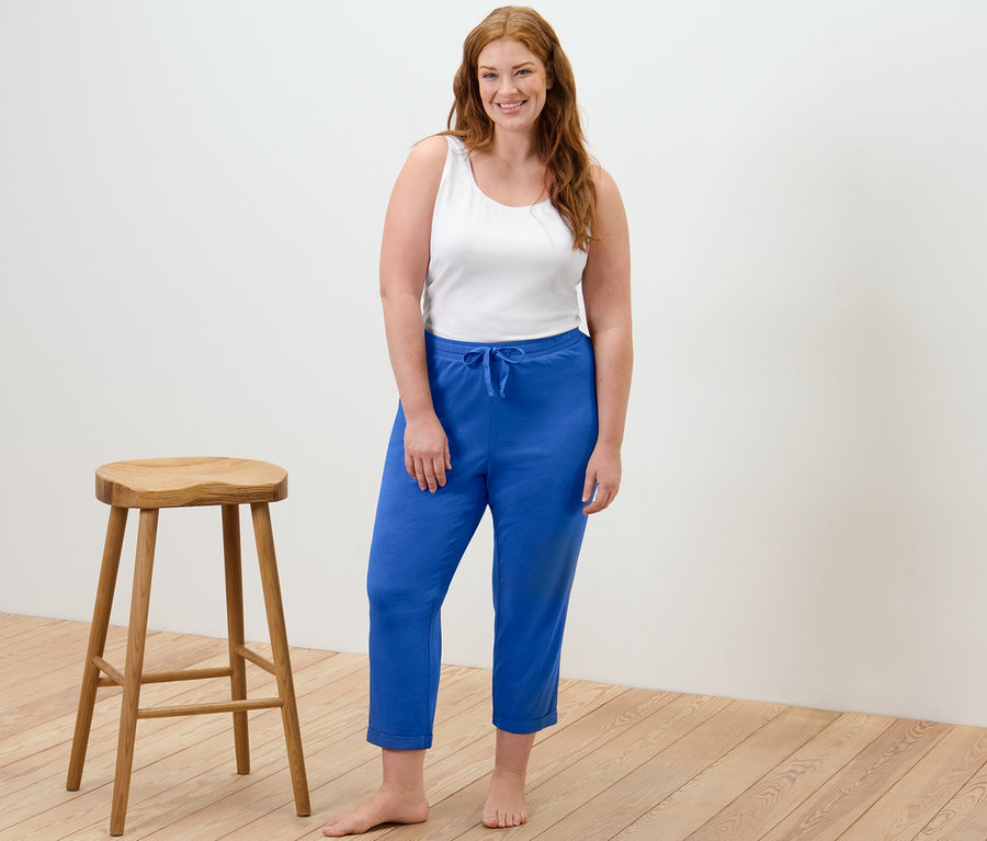 Une femme debout porte un caraco blanc et un pantalon de pyjama bleu.