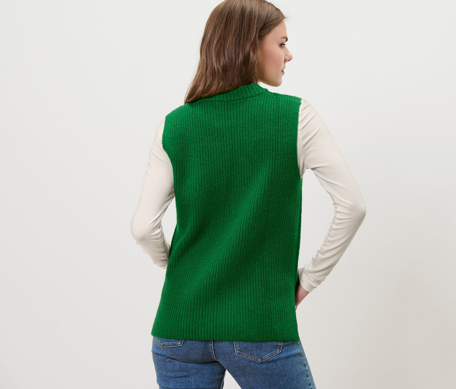 Une femme pose de dos et porte un pull sans manches en maille vert.
