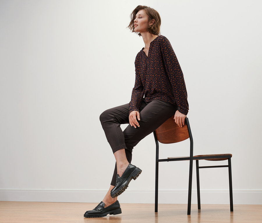 Une femme est assise sur une chaise et porte des mocassins en cuir, un pantalon en bengaline et une blouse imprimée.