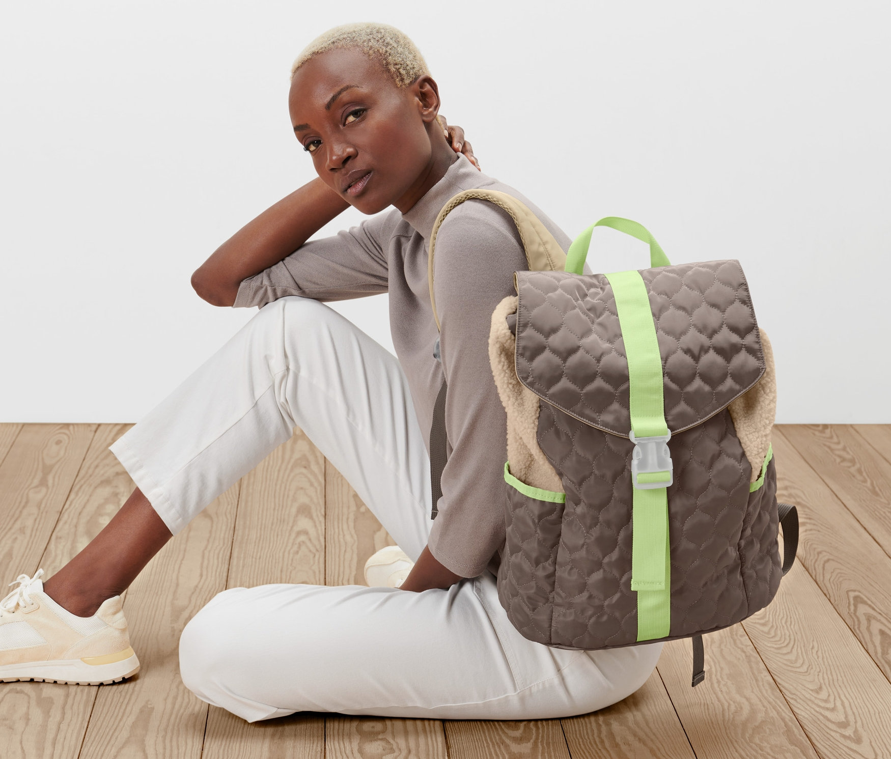 Femme assise par terre à côté d'un sac à dos aspect matelassé.