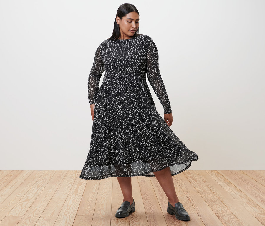 Femme en robe en mesh à pois et loafers en cuir debout sur un plancher en bois.