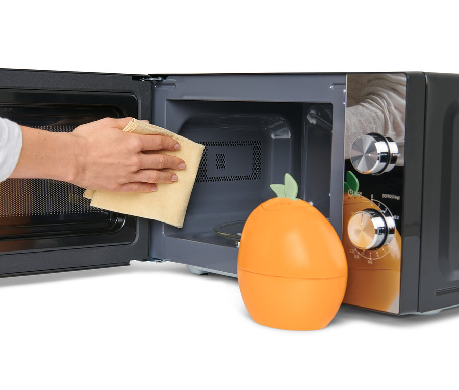 Une main essuie l'intérieur d'un micro-ondes avec un chiffon à côté d'un nettoyeur à micro-ondes en forme d'orange.