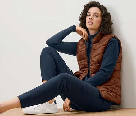 Femme assise par terre portant un gilet matelassé réversible.