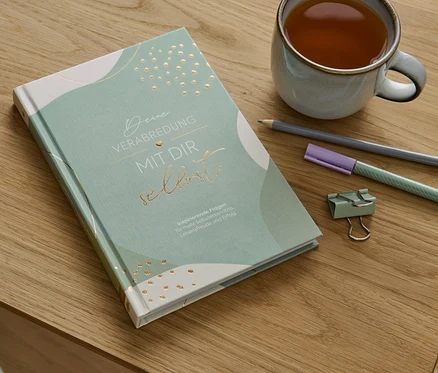 Sur une table en bois sont posés le livre «Deine Verabredung mit dir selbst» (Ton rendez-vous avec toi-même, en allemand), une tasse de thé, un crayon, un surligneur et un trombone.