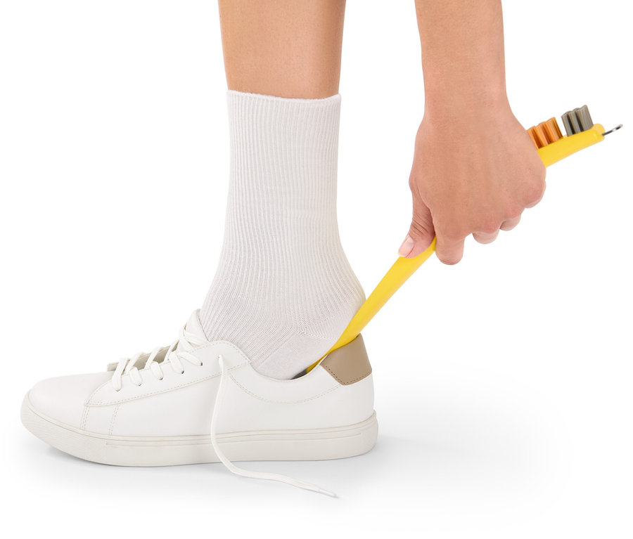 Une main tient une brosse à chaussures 3 en 1 jaune et nettoie une chaussure blanche avec.