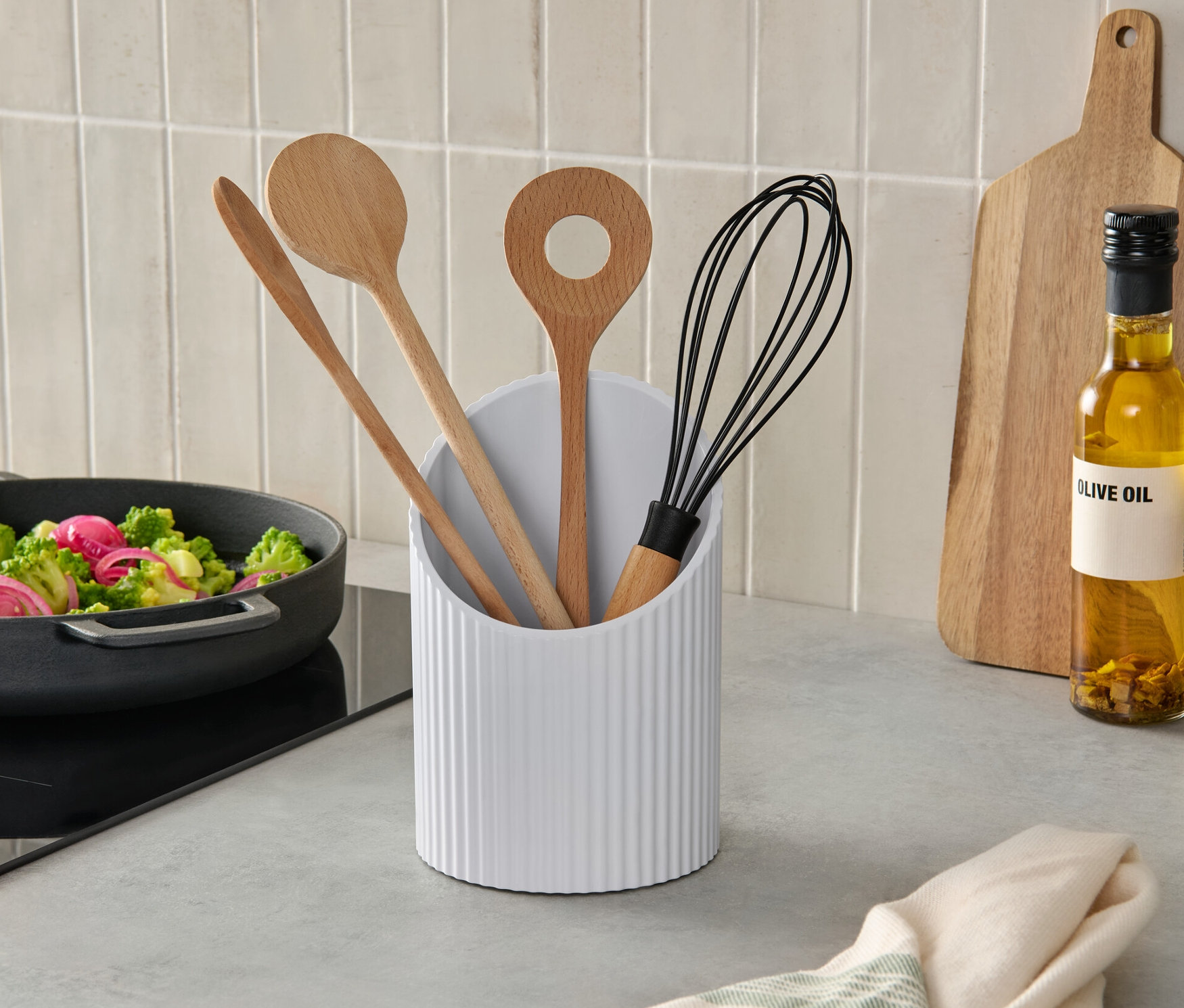 Dans une cuisine, une poêle de légumes est posée sur la plaque de cuisson à côté d'un support pour ustensiles contenant des cuillères en bois et un fouet.