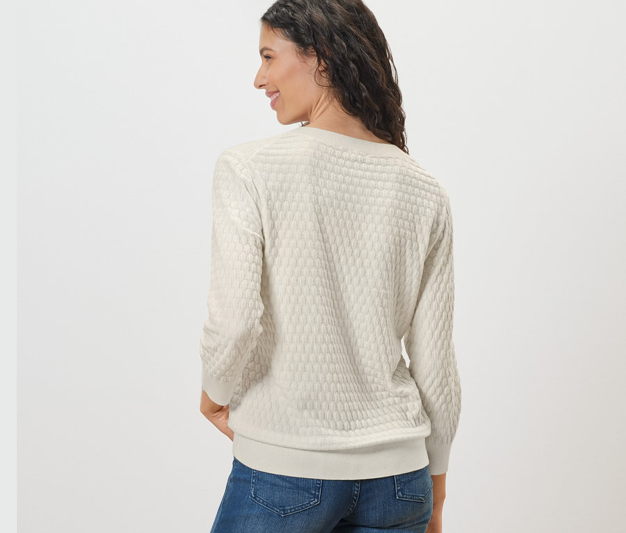 Une femme regardant par-dessus son épaule porte un pull-over en maille structurée et un jean.