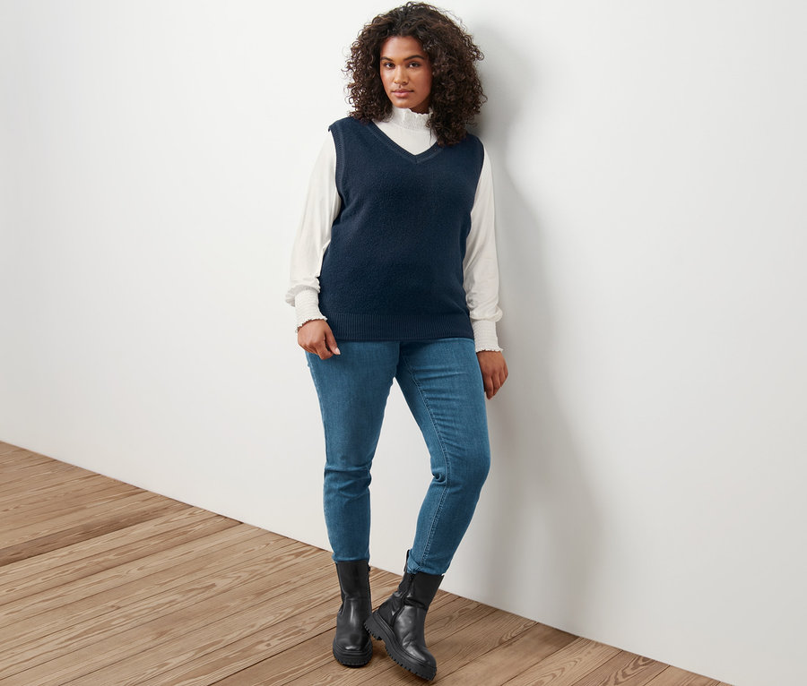 Femme posant en débardeur en maille aspect bouclé, blouse à col montant crème et tregging « Fit Nelly ».
