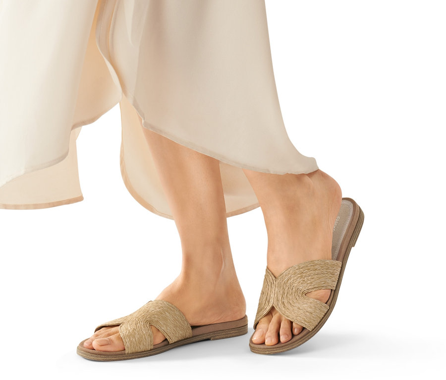 Jambes d'une femme portant des claquettes beiges.