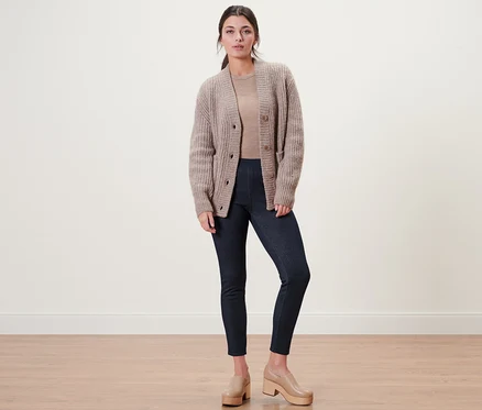 Une femme pose en legging doublé à l’aspect jean, cardigan et chaussures à plateforme marron clair.
