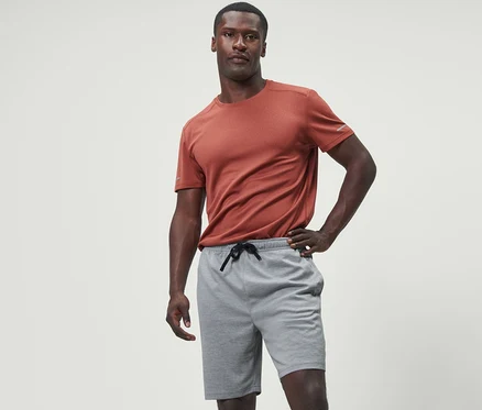 Homme posant en short de sport gris et t-shirt orange.