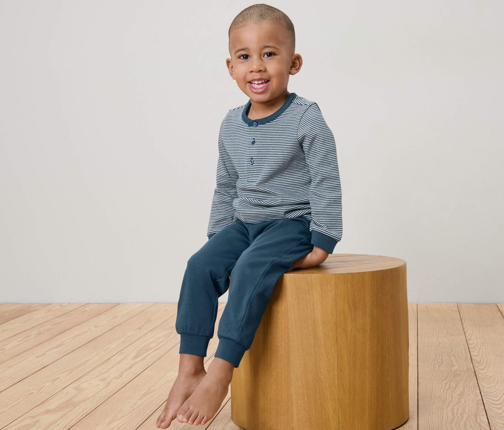 Un garçon est assis sur un tabouret en bois et porte un pyjama bleu pour enfant en maille interlock.