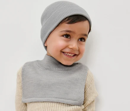 Un garçon souriant porte une écharpe-col roulé en laine et un bonnet.