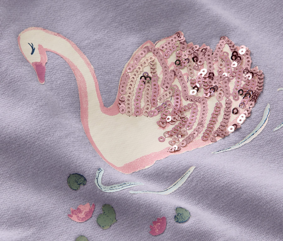 Gros plan sur une robe en sweat-shirt lilas pour enfant avec un motif de cygne orné de paillettes.