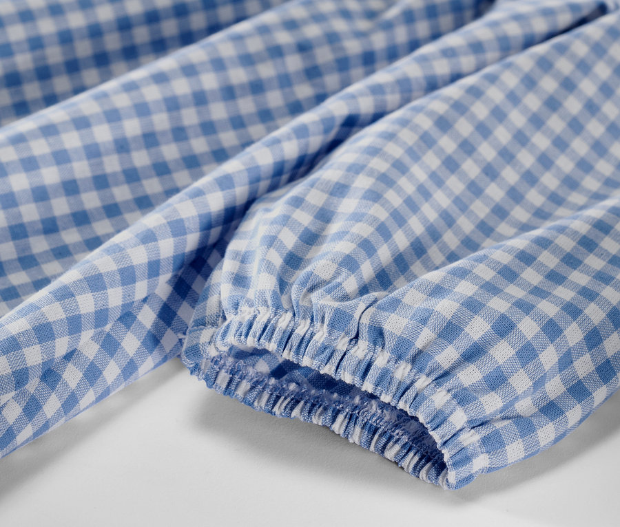 Gros plan sur une robe tissée pour enfant avec un motif à carreaux bleu et blanc et une manche longue.