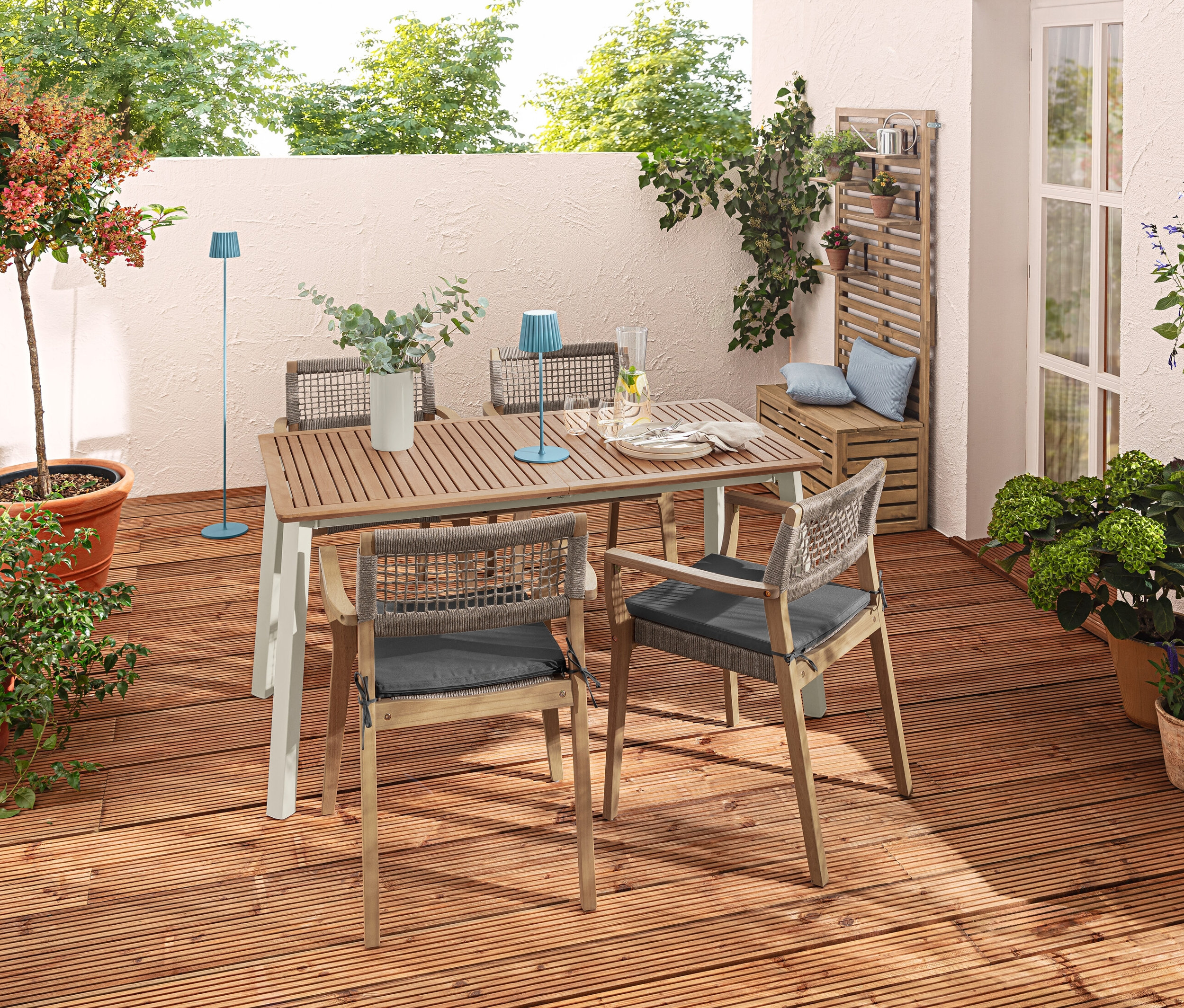 Terrasse extérieure avec table à rallonge « Liska », chaises empilables, lampe de table et lampadaire à LED rechargeables bleus et coussins d'extérieur.