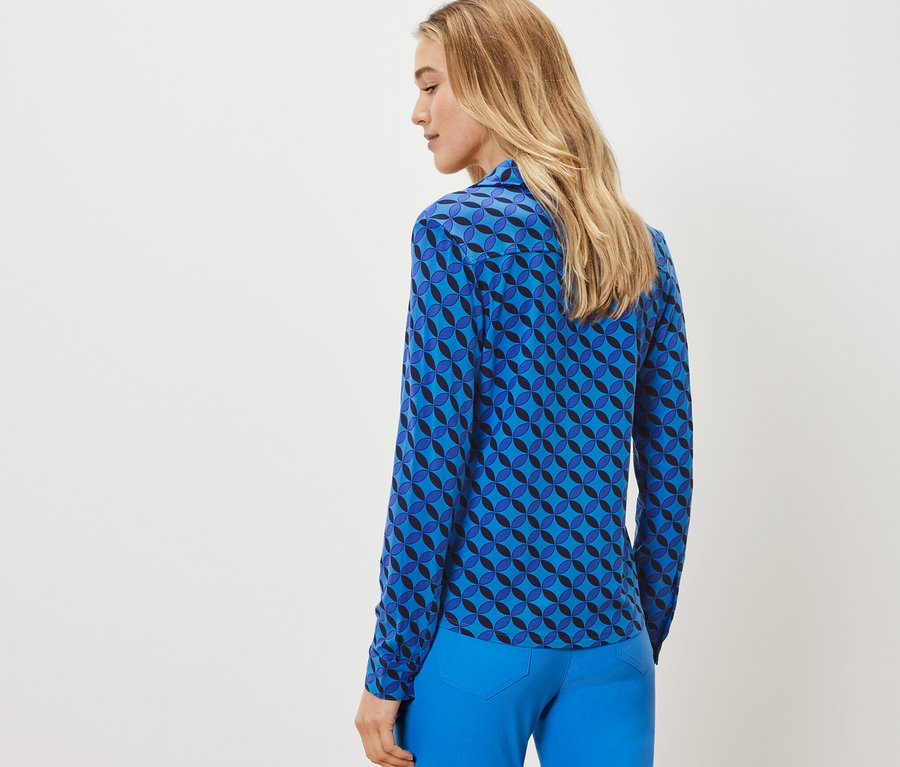 Une femme porte une blouse avec patte de boutonnage à motif géométrique.